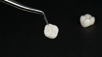 Closeup of tweezers grasping dental crown with black background