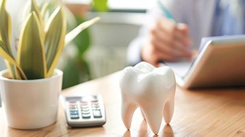 Large model tooth on table top with calculator, plant, and hand of person calculating something
