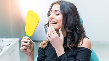 young woman admiring her new smile after getting dental implants in Longmont 