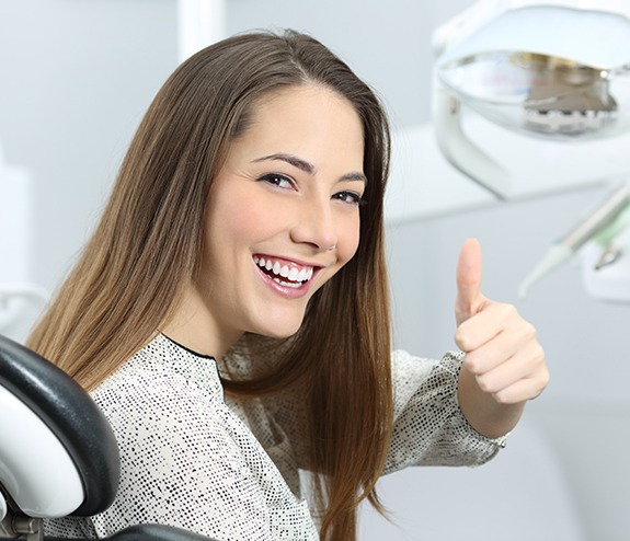 Woman smiling and giving thumbs up after teeth cleaning