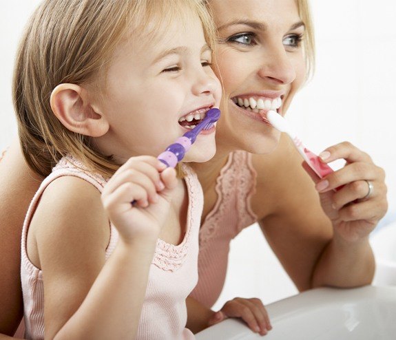 Mother showing daughter how to brush teeth