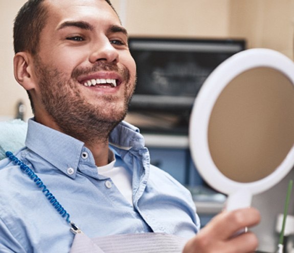 a patient looking in a handheld mirror at their teeth