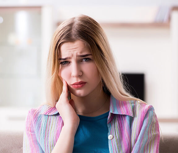 Woman with a dental emergency in Longmont touching her face