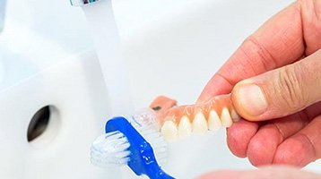 Person using a denture brush to clean their teeth