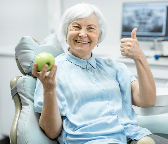 Woman smiling and holding an apple after denture tooth replacement