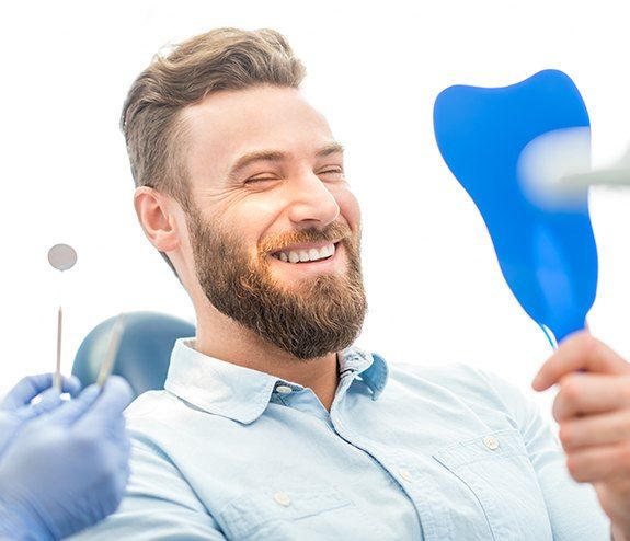 Man looking at smile after dental implant tooth replacement and improved oral hygiene