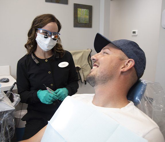 Man with dental implant replacement tooth smiling at dental team member