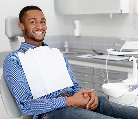 Man in dental exam chair smiling after dental implant tooth replacement