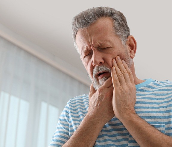 Man in need of tooth replacement holding jaw in pain