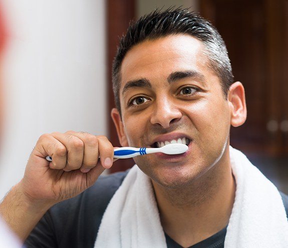 Man brushing teeth after dental implant supported bridge