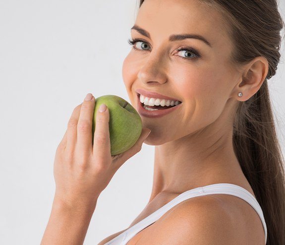 Woman eating an apple after replacing missing teeth with dental implants