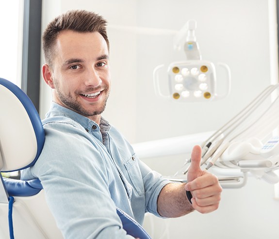 Man in dental chair giving thumbs up after dental implant tooth replacement