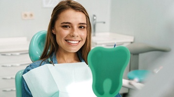 Female dental patient admiring her smile in a mirror after receiving dental implants in Longmont, CO