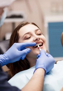 Woman with brown hair holding mirror as dentist holds shade guide to her teeth