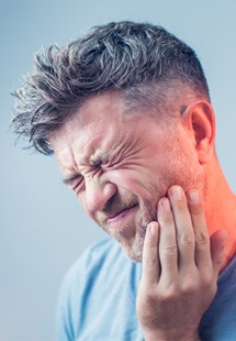 Man with gray hair squinting in pain holding hand to inflamed jaw