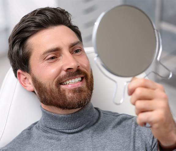 Man smiling in mirror after receiving CEREC crowns