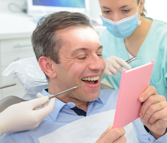 Man looking at smile after dental bridge tooth replacement