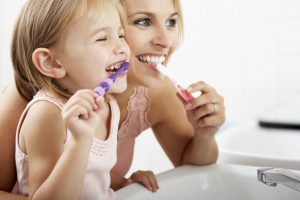 A mother and daughter brushing their teeth together.