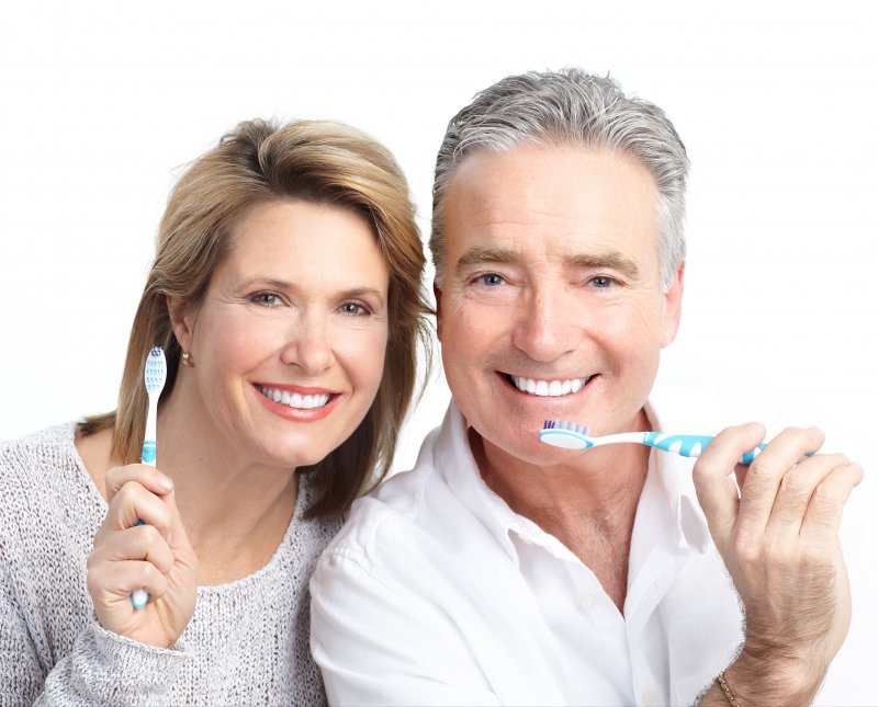 An older couple holding toothbrushes.